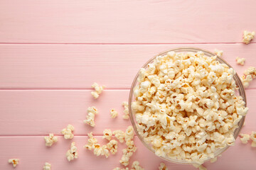 Popcorn in glass bowl on pink wooden background.