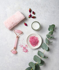 Organic pink sea salt with rose,  towel  and candle with eucalyptus branch on a white textured background. The concept of spa and wellness. Top view