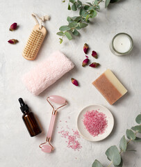 Fototapeta na wymiar Organic pink sea salt with rose, massage oil, soap, towel and a wooden brush on a white textured background. The concept of spa and wellness. Top view