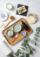 Fototapeta na wymiar the concept of organic cosmetics with clay, sea salt, soap, brush and eucalyptus branch in a wooden tray on a white textured background. Top view