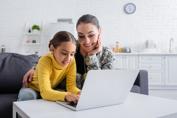 Smiling girl using laptop near mother in military uniform at home