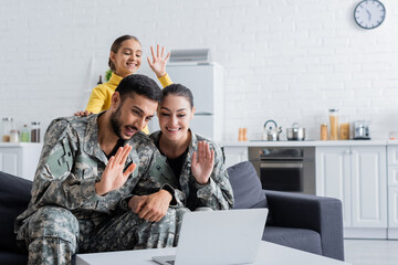 Happy parents in military uniform having video call on laptop near daughter at home