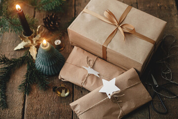Stylish christmas gifts wrapped in craft paper, candle, scissors, fir branches and bells on rustic...