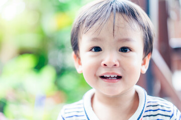 Happy baby toddler child showing front teeth with big smile and laughing: Dental milk teeth baby 1 year old.Happy face adorable asian male kid.nature green background.Asian child looking camera.