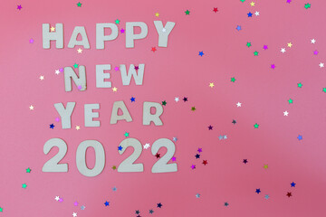 the inscription of wooden letters Happy New Year 2022 on a pink background and confetti in the shape of stars