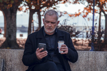 Fototapeta premium man sitting chatting with mobile phone while having coffee on autumn background