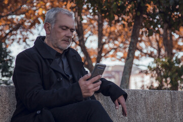 man in coat sitting using mobile phone
