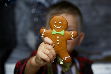 Adorable happy caucasian child with gingerbread and makes a funny face expression. Selective focus. Atmospheric, aesthetic Christmas home for New Year's Eve. Cheerful baby boy. Joyful, good mood