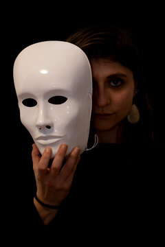Portrait of woman with mask in her hand. Concept of hypocrisy or double personality. Black background