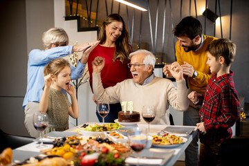 Family celebrating grandfather birthday with cake and candles at home