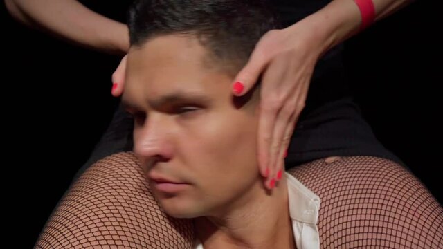 Portrait male dancer with woman in fishnet stockings sitting on his shoulders Her hands control the man turning his head from side to side.Concept of avoiding control,reaching compromise