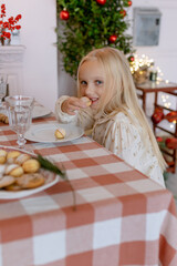 Child girl sitting at the Christmas table eating sweets