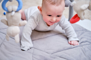 Happy infant baby is playing lying on a mat with toys suspended over it