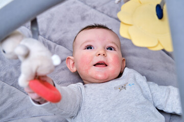Happy infant baby is playing lying on a mat with toys suspended over it