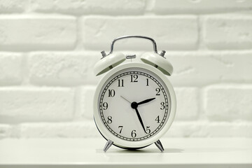 White alarm clock with black dial on brick wall background