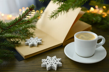 Obraz na płótnie Canvas Christmas or winter coffee. Coffee cup, book, Christmas tree and Christmas lights, golden bokeh, blurred background. Atmosphere of winter festive and black coffee, hot aroma drink at a christmastime