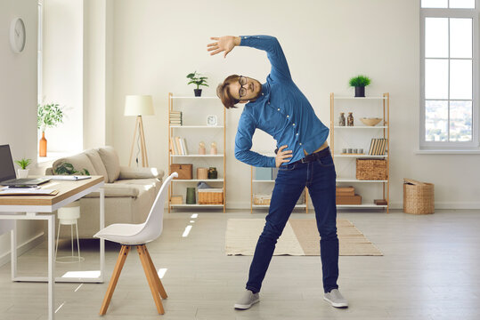 Man Having Sports Workout At Work Or At Home. Fit Young Guy Doing Morning Exercise In Office Workplace. Student Or Remote Employee Enjoying Warm Up Fitness Stretching Before Productive Day