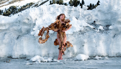 Fototapeta na wymiar Young sexy blonde naked woman in winter, stylishly hidden by creative, dry, dried banana tree stands in the snow, freezes, accusing the world of climate change