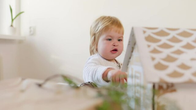 A little smiling girl is decorating a cardboard house. Slow motion. Preparations for Christmas.
