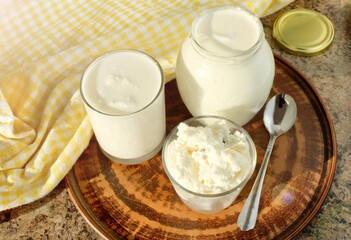 Close-up of a glass jar and a glass with sour milk and a bowl with cottage cheese and raisins....