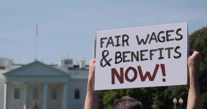 WASHINGTON, DC - Circa March, 2021 - A man waves a handmade FAIR WAGES AND BENEFITS NOW! protest sign outside the White House.  	