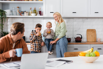 kids drinking orange juice near happy mom and father freelancer working on blurred foreground