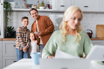 happy man with kids near wife working in kitchen on blurred foreground