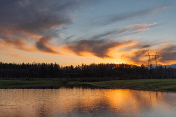 Obraz premium reflections of colored clouds in the lake water at sunset,silhouettes of trees in golden hour
