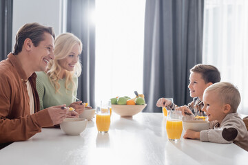 happy parents and sons talking while eating tasty corn flakes for breakfast