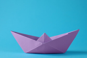 Handmade violet paper boat on light blue background. Origami art
