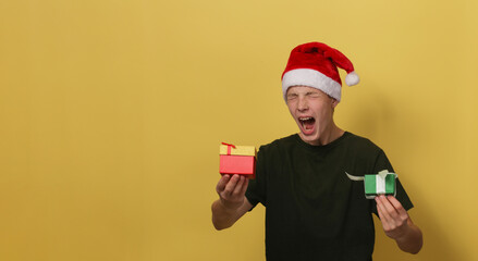 A happy boy in a Santa hat and a green T-shirt is holding a gift against a blue background.
