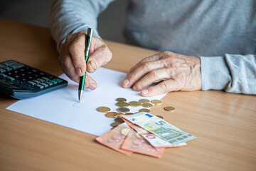 Fototapeta na wymiar Hands of old senior man with calculator and bills counting euro money at home.