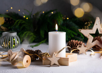 White advent candle on wooden box with christmas lights, cones, wooden star.