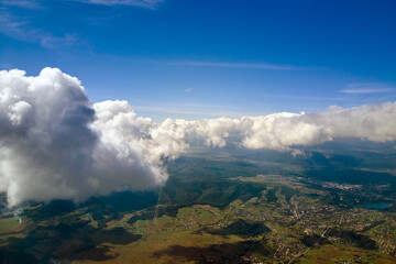 Aerial view from airplane window at high altitude of distant city covered with puffy cumulus clouds...