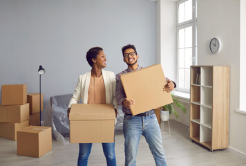 Fototapeta na wymiar Moving to new house together. Portrait of cheerful young African American couple in love moving into new home. Man and woman holding cardboard boxes with personal belongings and having fun.