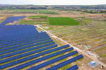 Fototapeta na wymiar Aerial view of big electric power plant construction with many rows of solar panels on metal frame for producing clean ecological electrical energy. Development of renewable electricity sources