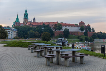 Four tables with benches on the river bank and in the background the Wawel Royal Castle in Krakow.