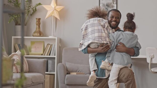 Slowmo shot of two cheerful little girls running to their African-American father for hugging at cozy home