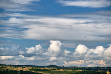 Bright landscape of white puffy cumulus clouds on blue clear sky over rural area.