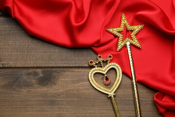 Different golden magic wands and red fabric on wooden table, flat lay. Space for text