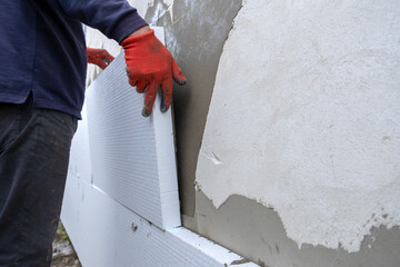Construction worker installing styrofoam insulation sheets on house facade wall for thermal...
