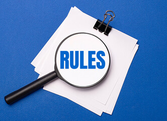 On a blue background, white sheets under a black paper clip and on them a magnifying glass with the...