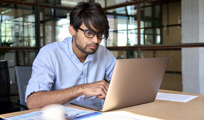 Young Indian businessman entrepreneur wearing glasses using computer working online, e learning,...