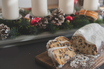 Traditional Christmas stollen made of dried fruits and nuts sprinkled with powdered sugar on the background of a Christmas decor with candles. Traditional Christmas cupcake