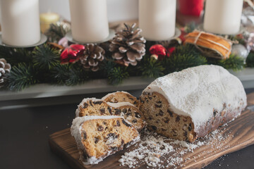 Traditional Christmas stollen made of dried fruits and nuts sprinkled with powdered sugar on the background of a Christmas decor with candles. Traditional Christmas cupcake.