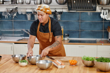 Portrait of tattooed woman cooking vegetables in kitchen interior, copy space