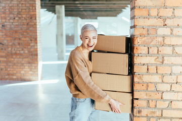 Middle age enjoy business woman carrying cardboard boxes for moving into a new office in the empty open space with loft interior on background. New opportunities concept.