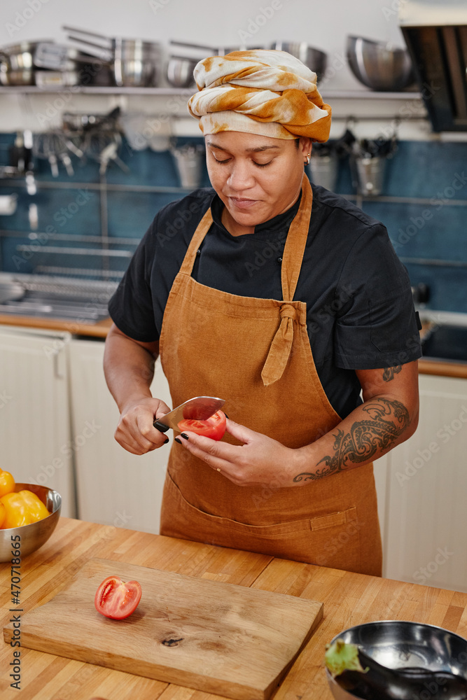 Wall mural vertical portrait of tattooed woman cooking vegetables in kitchen interior