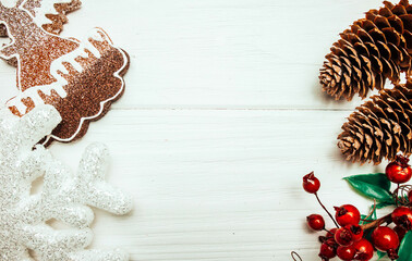 Pine cones, red berries and christmas decorations on white wooden background	