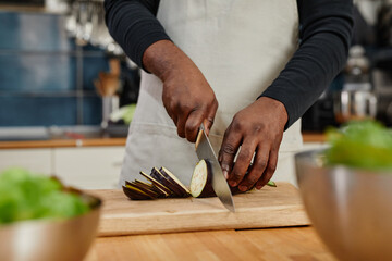 Close up of unrecognizable African-American man cutting aubergine while cooking dinner at home,...